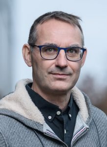 Man with glasses against a blurred background.